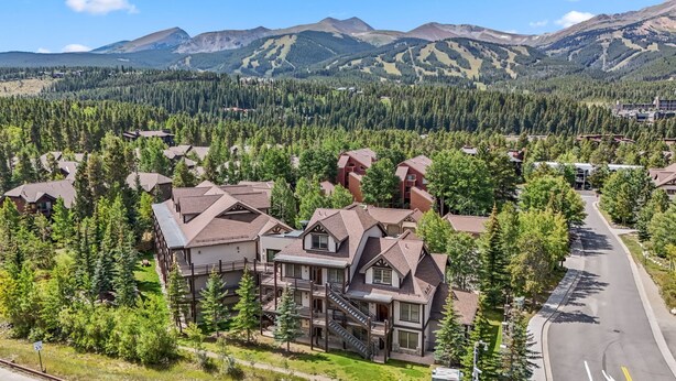 A residential area with a prominent house featuring a large balcony and multiple floors, surrounded by dense forest and mountains in the background. - Mountain Escape | Hot Tub + Walk to Town (Breckenridge)