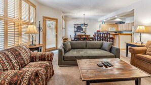 A living room with a sofa, a patterned armchair, a coffee table, and a dining area with a table and chairs. - Mountain Escape | Hot Tub + Walk to Town (Breckenridge)