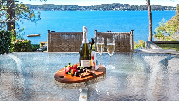 A table with a bottle of wine, two glasses, and a wooden board with strawberries and chocolate. - Catalina Bay - Absolute Lakefront - Jetty - Boat house on waters edge (Fishing Point)