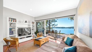 A modern living room with a large TV, bookshelves, a sofa, and a view of the sea. - Catalina Bay - Absolute Lakefront - Jetty - Boat house on waters edge (Fishing Point)