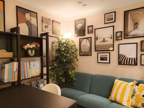 A cozy living room with a bookshelf, a green sofa, and various framed pictures on the walls.