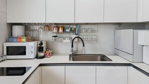 Una cocina moderna con armarios blancos, microondas integrado, lavaplatos y refrigerador.