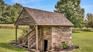 A rustic stone building with a wooden staircase leading to a door, surrounded by a grassy field and trees. - Historic Farmhouse with Pool & Hot Tub in Wine Country, Near Washington, DC (Hamilton)