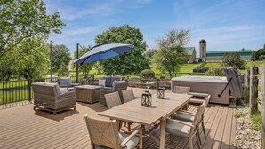 An outdoor deck with a table and chairs, a large umbrella, and a hot tub. - Historic Farmhouse with Pool & Hot Tub in Wine Country, Near Washington, DC (Hamilton)