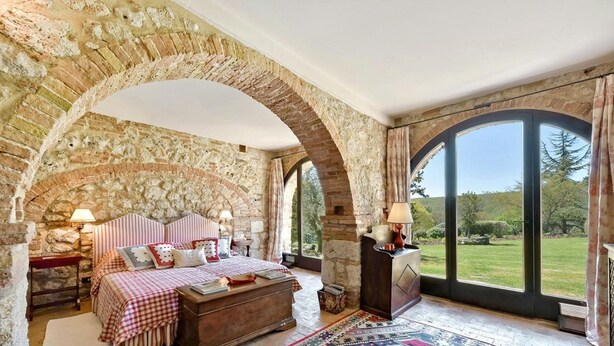 A bedroom with a stone arch, a bed with checkered bedding, a nightstand, and a view of the outdoors. - Luxurious independent villa with 12 beds in Val d'Orcia (Sarteano)