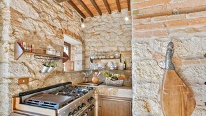 A rustic kitchen with stone walls, a gas stove, wooden cabinets, and shelves with jars and plants. - Luxurious independent villa with 12 beds in Val d'Orcia (Sarteano)