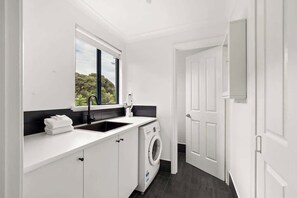 A compact laundry room with a washing machine, a sink, and a window.
