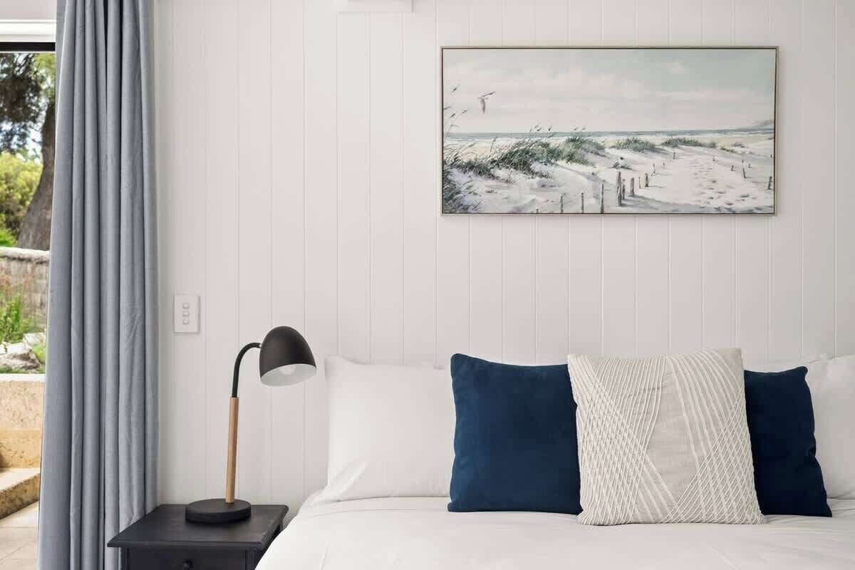 Ein Schlafzimmer mit einem Bett, einem Nachttisch, einer Lampe und einem Bild an der Wand.