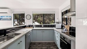 A modern kitchen with a built-in oven, a sink, and a window overlooking a garden. - Surfers Paradise—Oceanview Garden Beach House (Yallingup)