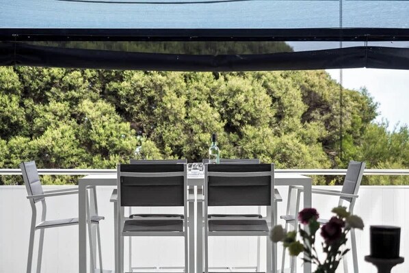 A balcony with two chairs and a table, a bottle on the table, and a view of trees.