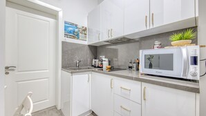 Une cuisine moderne avec des meubles blancs, un four à micro-ondes, un évier et une petite plante posée sur le plan de travail.