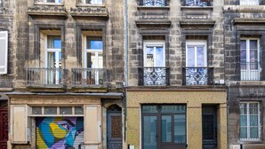 Un bâtiment avec une porte de garage fermée, une grande fenêtre et une porte ornée d’une grille métallique décorative.