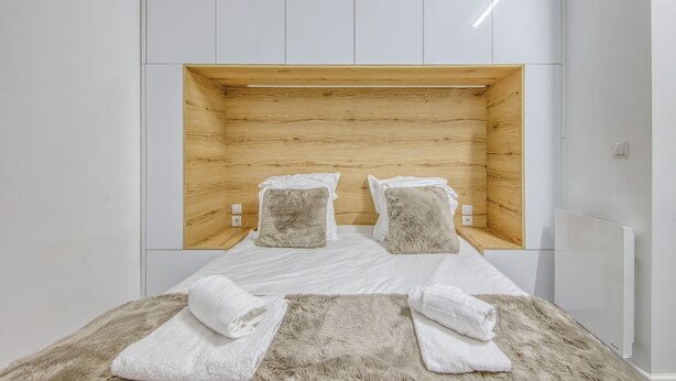 Une chambre d’hôtel moderne avec une tête de lit en bois, du linge de lit blanc et un plaid en fourrure sur le lit.