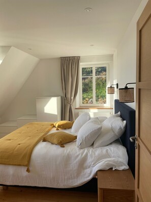 A bedroom with a bed, a window with curtains, a bedside table, and a lamp. - Holiday Home 'Bréhat - Villa San Denn' with Sea View, Private Garden and Wi-Fi (Île-de-Bréhat)
