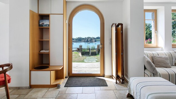 Habitación con una estantería empotrada de madera, una puerta que da a un área exterior, una cama con ropa de cama a rayas y una ventana con vistas al exterior.