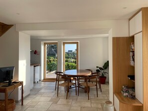 A modern kitchen with a dining area, a TV, and a view of the garden. - Holiday Home 'Bréhat - Villa San Denn' with Sea View, Private Garden and Wi-Fi (Île-de-Bréhat)