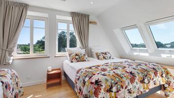 Un dormitorio con cama, dos ventanas, tragaluz y vistas al exterior con vegetación.
