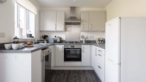 Una cucina moderna con mobili bianchi, una cappa aspirante in acciaio inossidabile, un forno integrato e un frigorifero.