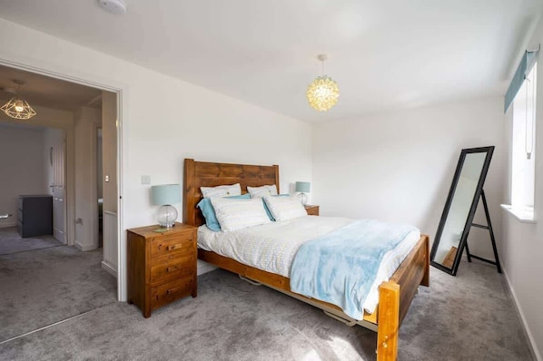 A bedroom with a wooden bed, bedside lamps, a dresser, and a full-length mirror.