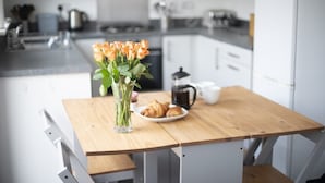 Una cucina con un tavolo di legno, un vaso di fiori, un piatto di croissant e una macchina per il caffè.