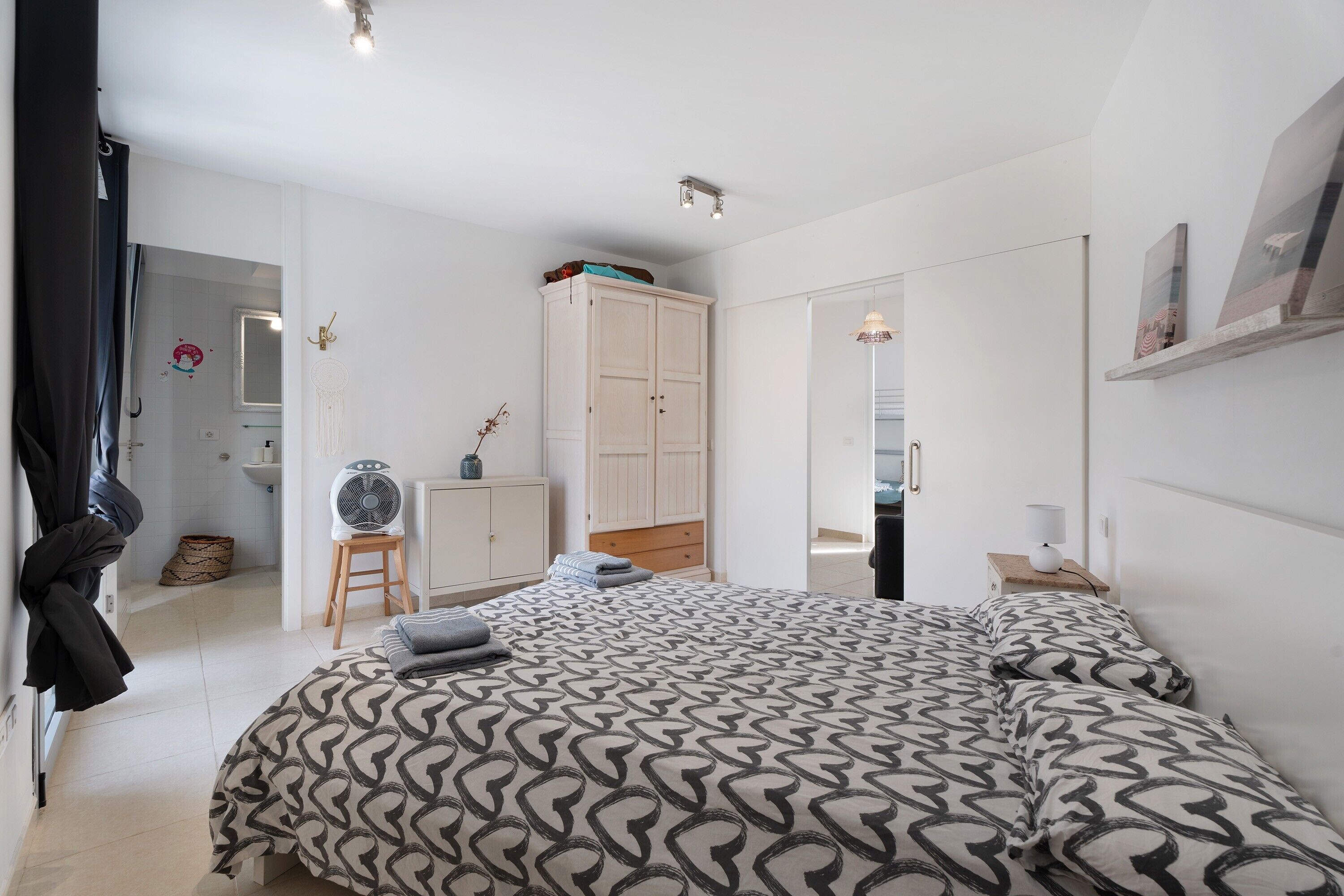Un dormitorio con edredón estampado, un armario, una mesita de noche con lámpara y un espejo.