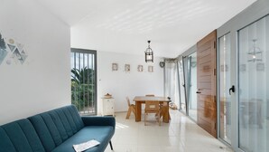 A modern living room with a sofa, dining table, and chairs, a small cabinet, and a glass door leading outside. - Vacation Home 'Villa En Taro' with Sea View, Private Terrace and Wi-Fi (Güímar)