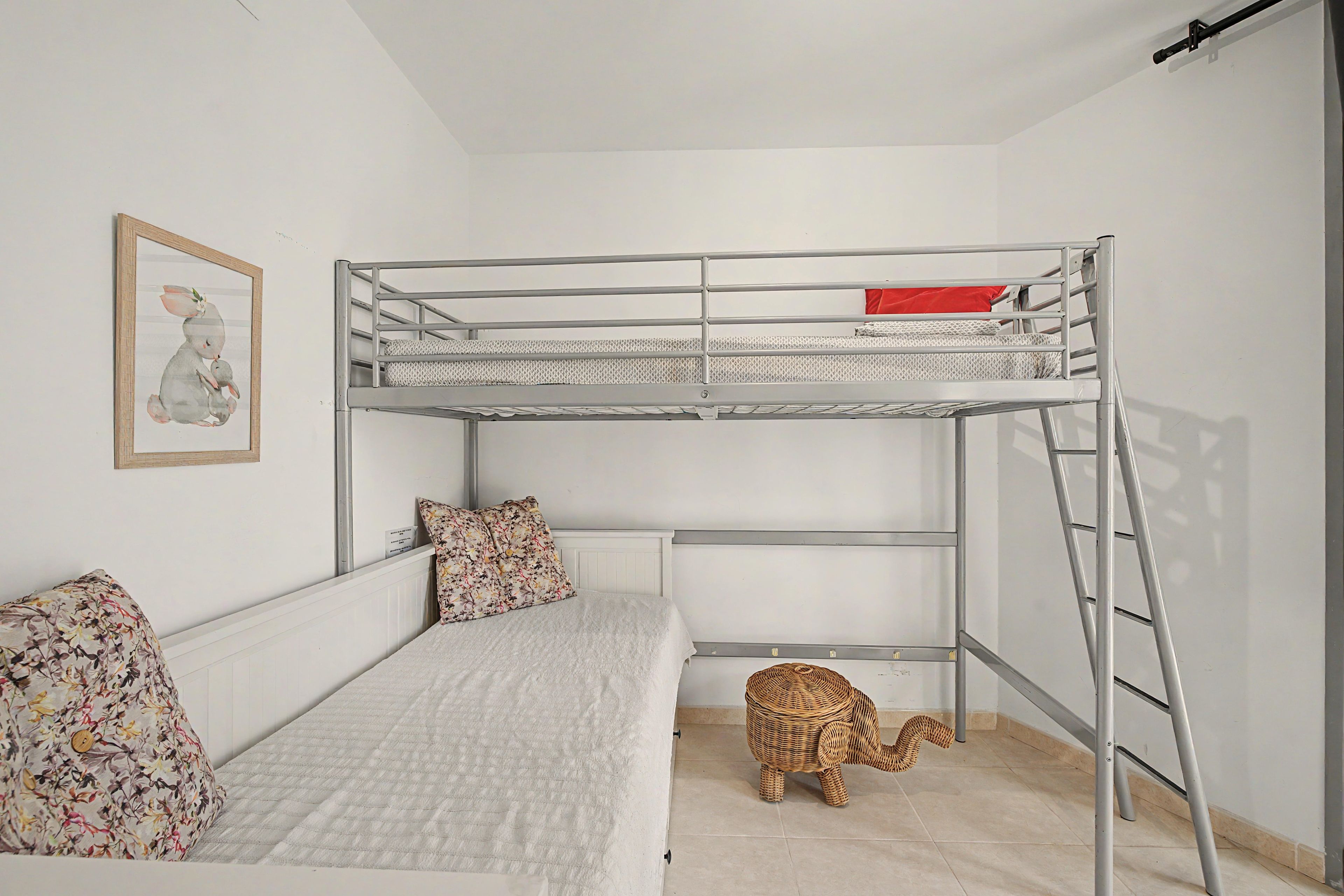A bunk bed with a ladder, a small wicker toy, and a framed picture on the wall.