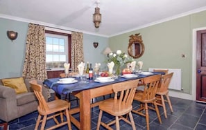 A dining room with a wooden table set for four, surrounded by wooden chairs. - Coastal Farmhouse | Sea Views | Ideal for Groups (Pembrokeshire)