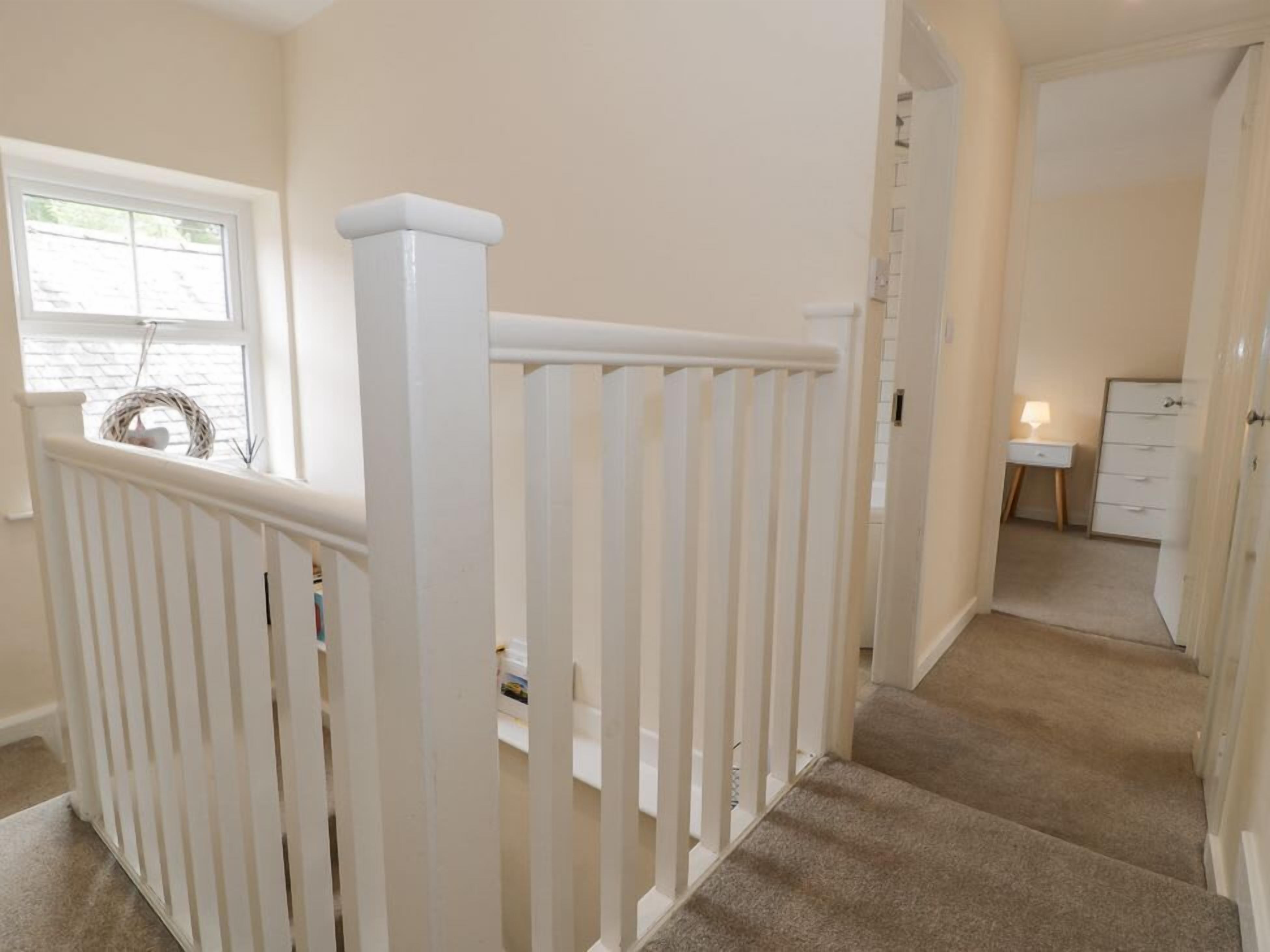 A staircase with white railings leading to a bedroom with a white dresser and a small bedside table.