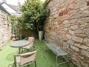 A patio with a stone wall, a metal bench, wicker chairs, and a round table. - Pet-Friendly Stay Near Ruthin Castle with Parking (Ruthin)