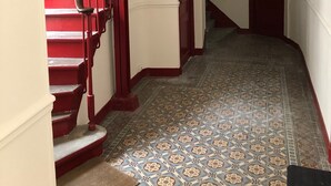 A hallway with a red staircase, patterned floor tiles, and a door at the end.