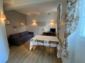 A compact living space with a sofa, a dining table, a TV, and wall-mounted lights.