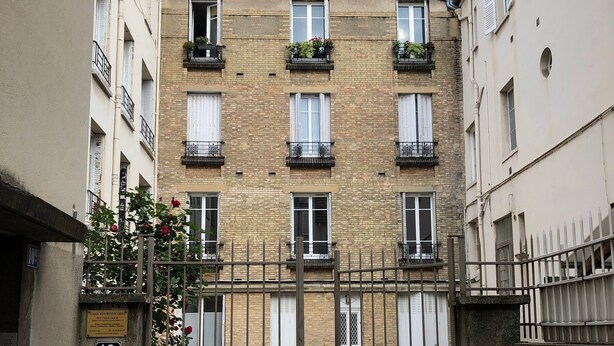 A gated entrance to a building with multiple windows and balconies, a sign indicating '10', and a small sign above the gate.