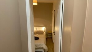 A narrow hallway leading to a bedroom with a bed, bedside table, and a lamp.