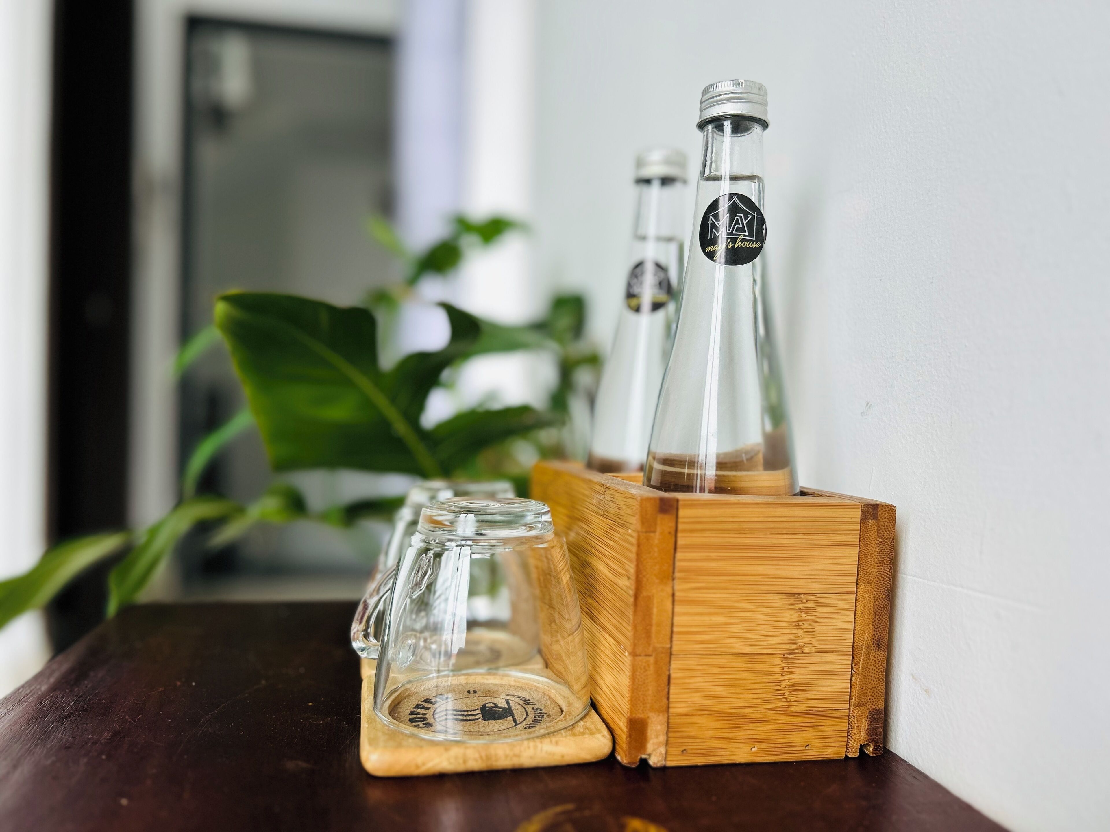 A wooden bottle holder with three glass bottles on a dark wooden surface.