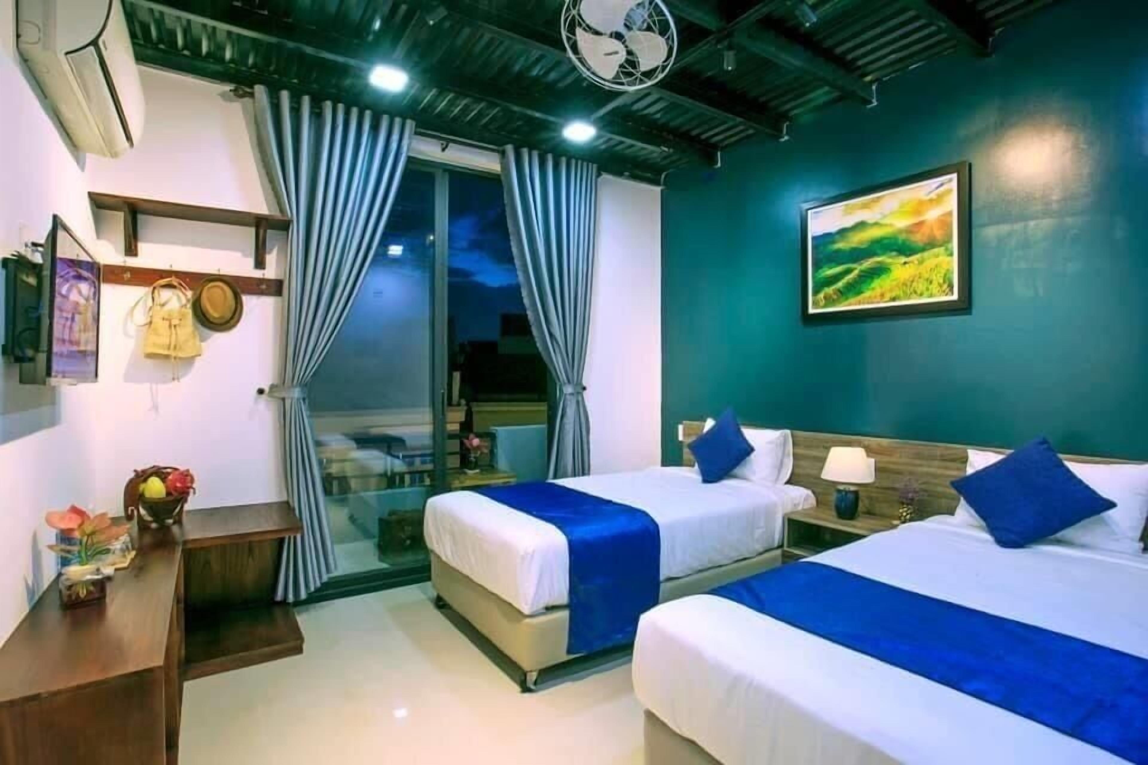 A hotel room with two beds, a desk, and a window with curtains.