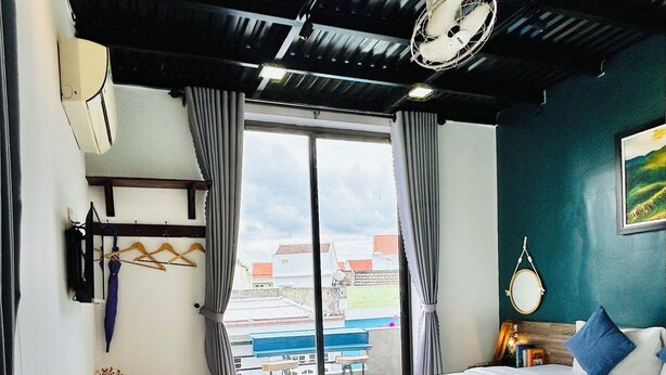 A hotel room with a large bed, a desk with a chair, a potted plant, and a view of the outside. - May's House Hoi An Ancient Town Center (Da Nang)