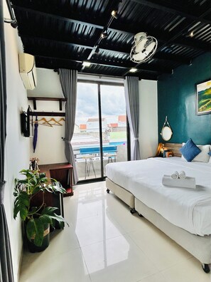 Ein Hotelzimmer mit einem großen Bett, einem Schreibtisch mit Stuhl, einer Zimmerpflanze und Blick ins Freie.