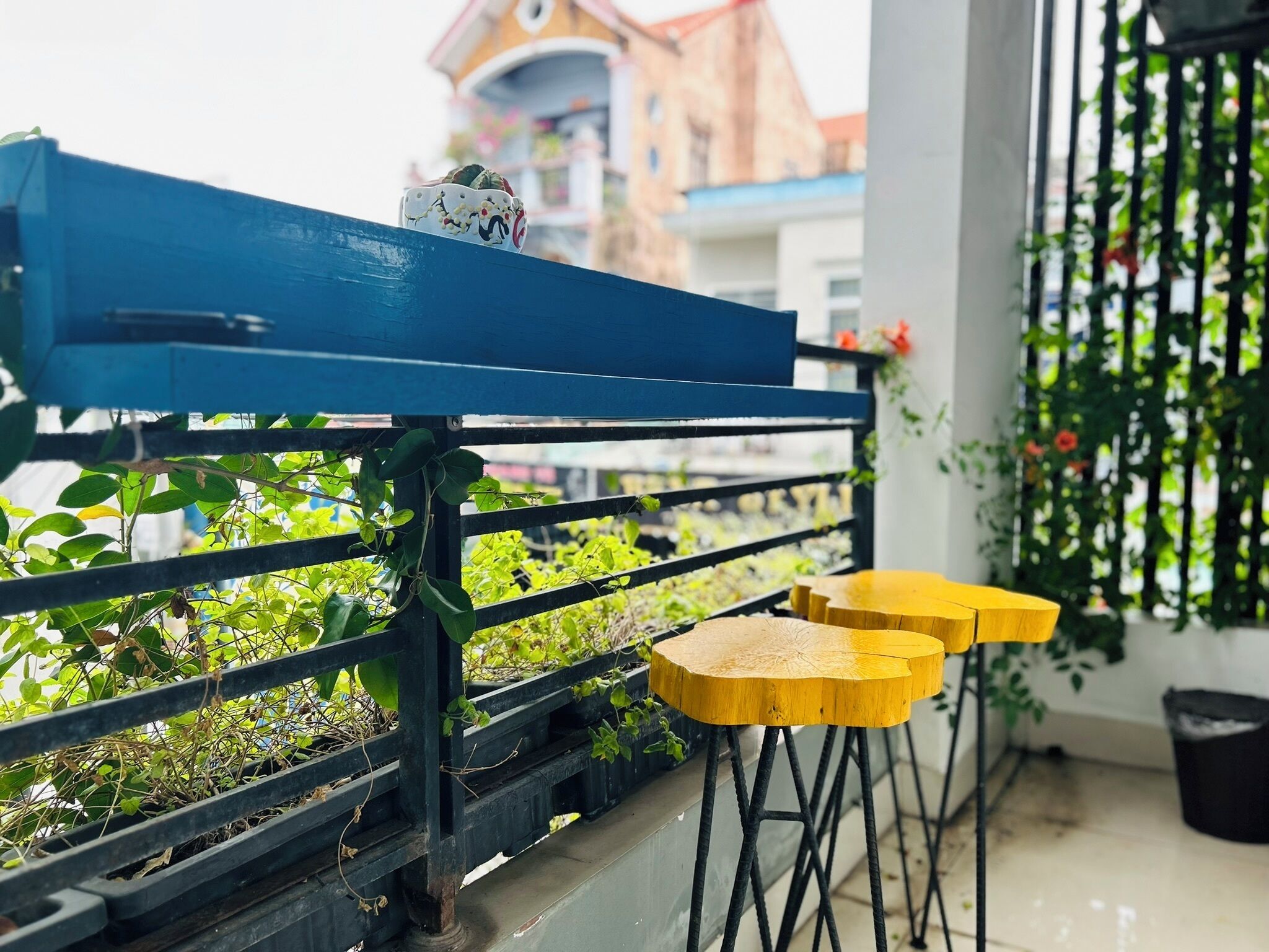 Um banco azul com um objeto decorativo, rodeado por vegetação e um banquinho amarelo.