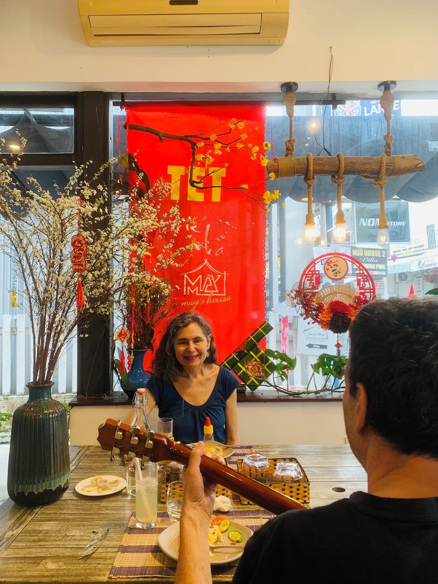 A dining area with a table set for two, a red banner with Chinese characters, and a view of the street outside.