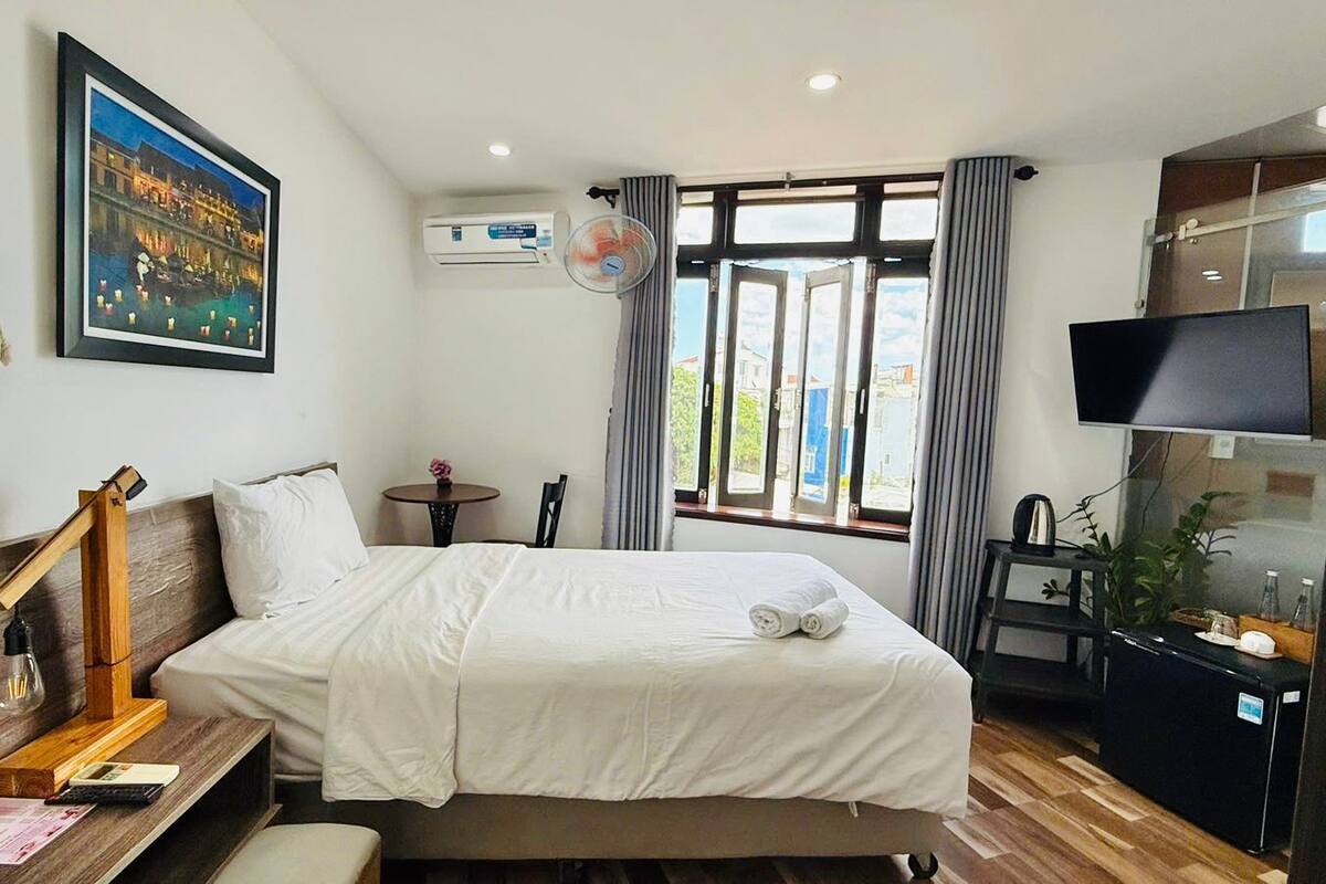 A hotel room with a bed, a desk with a lamp, a TV, and a window with curtains.