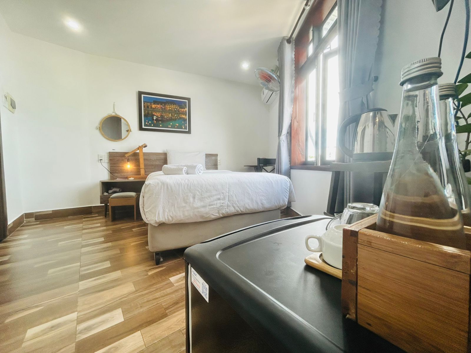Une chambre d’hôtel comprenant un lit, une table de chevet, une chaise, un bureau et une fenêtre avec des rideaux.