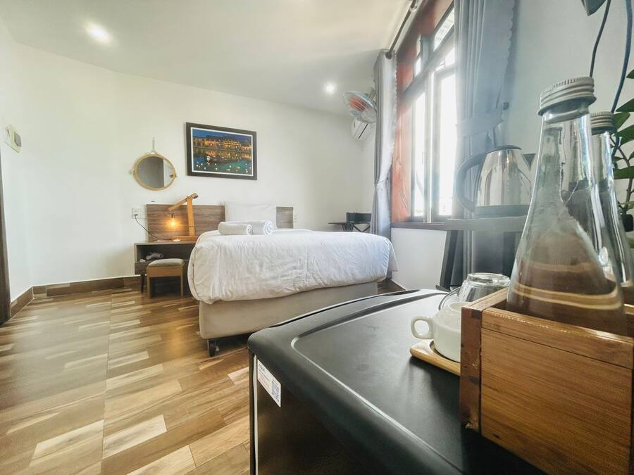 Ett hotellrum med en säng, ett nattduksbord, en stol, ett skrivbord och ett fönster med gardiner.