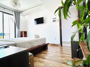 A hotel room with a bed, a TV mounted on the wall, a wooden floor, and a large window with curtains. - May's House Hoi An Ancient Town Center (Da Nang)