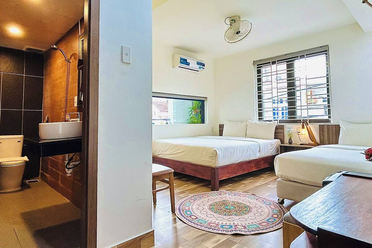 A room with a bed, a desk, a window, a wall-mounted air conditioner, and a shower area.