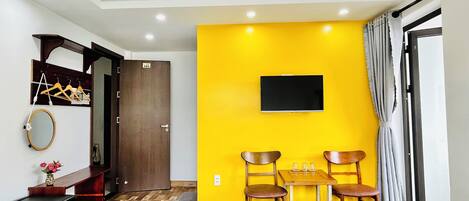 Une chambre d’hôtel avec deux lits, un plancher en bois, un mur d’accent jaune, un téléviseur fixé au mur et une petite table avec des chaises.