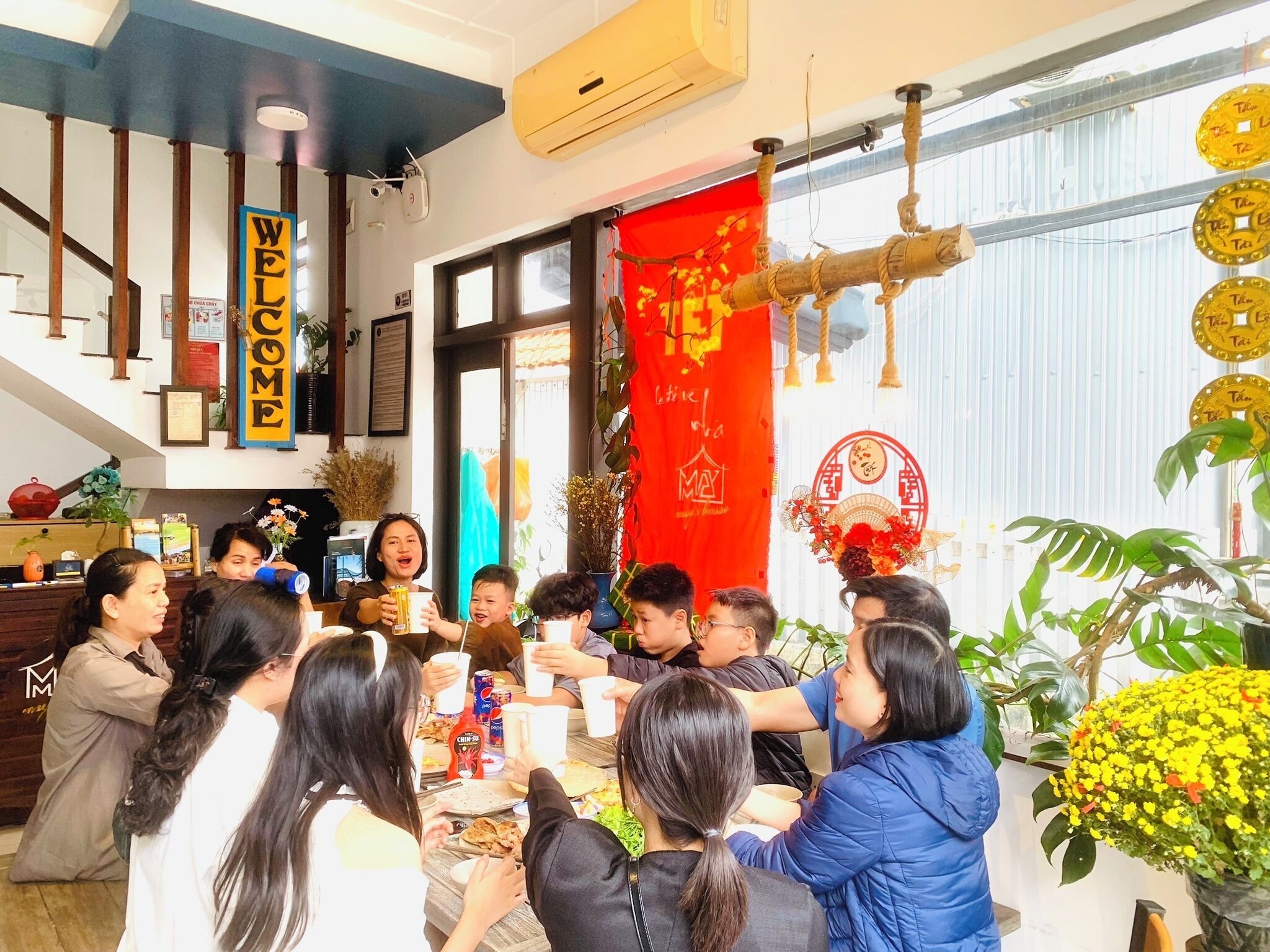 Un grupo de personas reunidas alrededor de una mesa en una sala bien iluminada, con un estandarte rojo y decoraciones tradicionales.