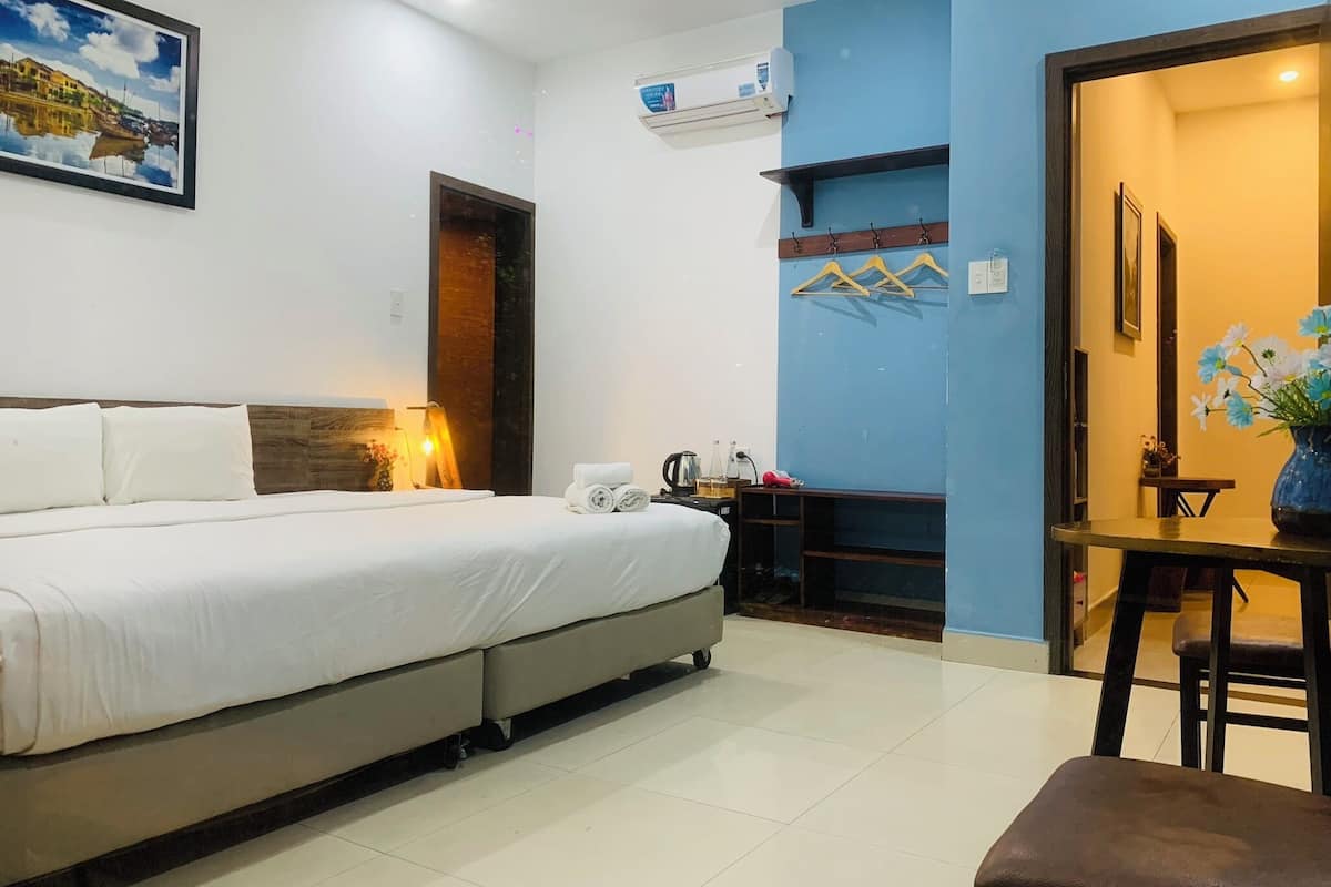 A hotel room with a bed, a desk, a chair, a table with flowers, and a painting on the wall.