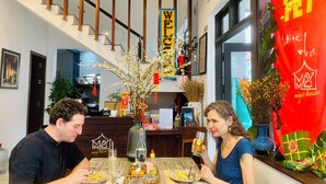 A dining area with a wooden table, a 'WELCOME' sign, and a red decoration with Chinese characters. - May's House Hoi An Ancient Town Center (Da Nang)