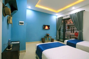 A hotel room with two beds, a TV, a small table with a fruit bowl, and a view of a building through a glass door. - May's House Hoi An Ancient Town Center (Da Nang)